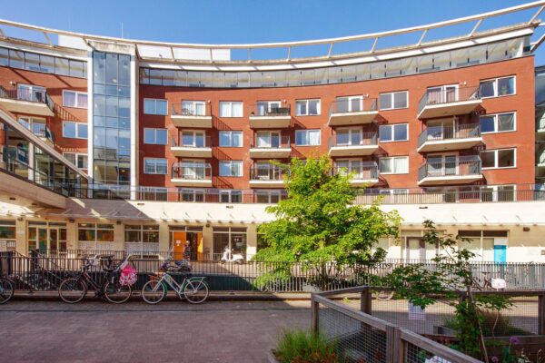 Appartementencomplex Harriet Freezerhof met balkonnetjes, fietsenstalling en groene binnenplaats op een zonnige dag.